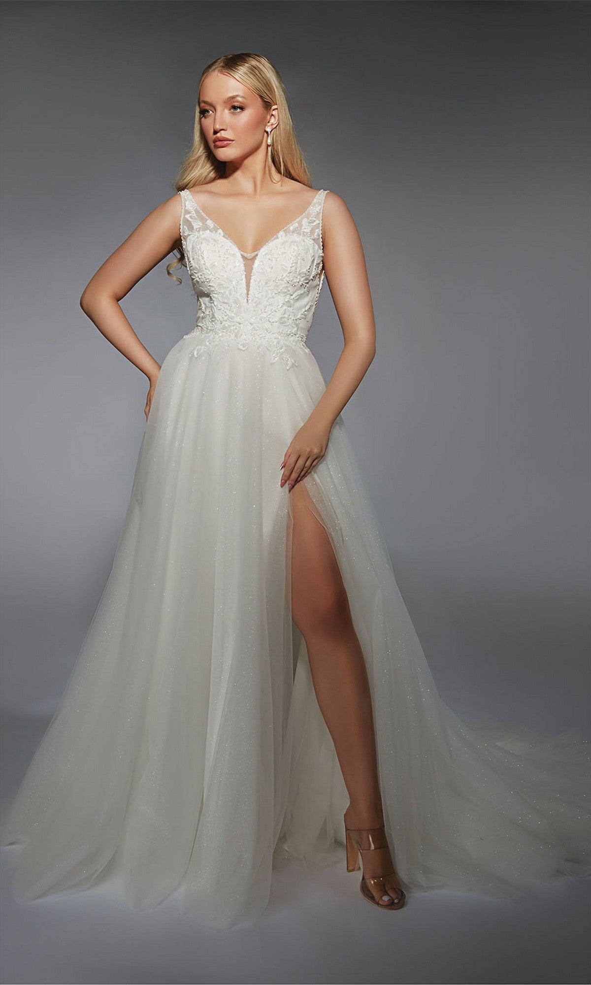A woman models the Alyce 7125 long ivory dress, featuring a sleeveless design, plunging neckline, lace bodice, and high-slit tulle skirt against a gray background—an elegant choice for any formal evening occasion.